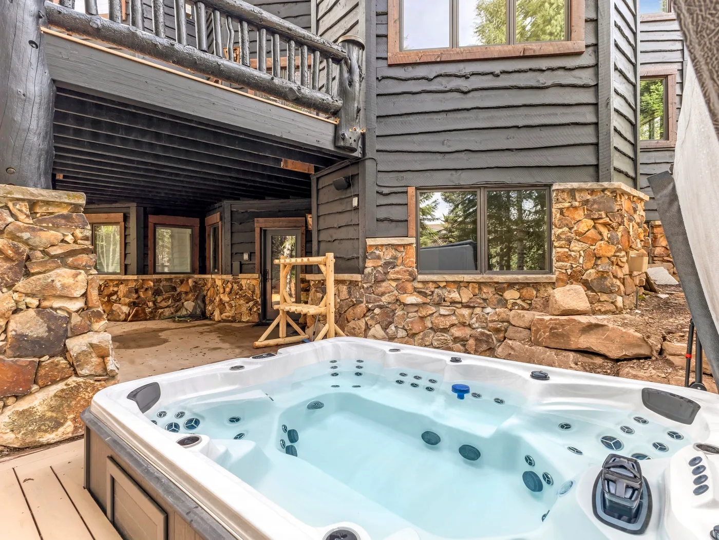 An outdoor hot tub sits beside a rustic building with stone walls and wooden siding.