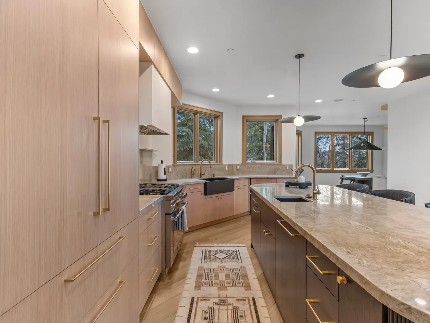 A bright kitchen with light wood cabinetry, a large island, and windows overlooking trees.