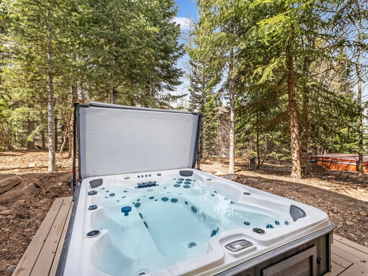 An outdoor hot tub sits on a wooden deck among tall trees.