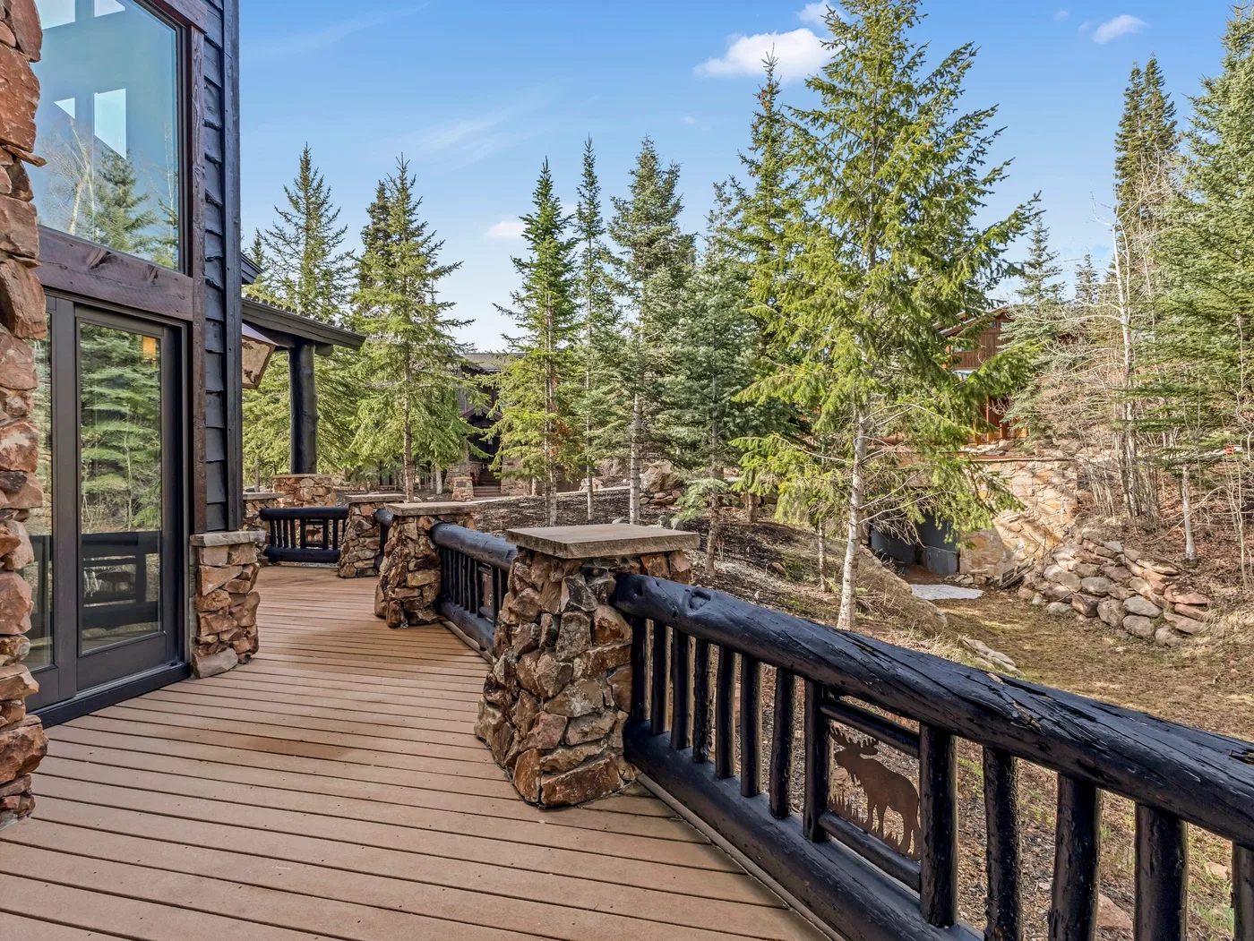 A wooden deck overlooks a wooded outdoor scene with evergreen trees.