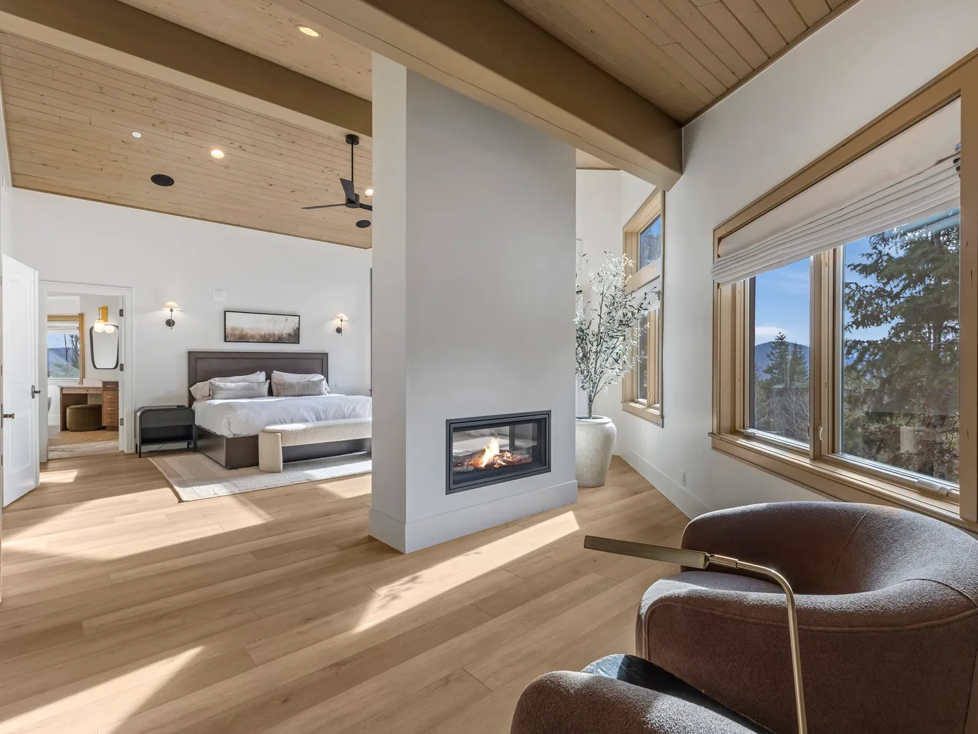 A bedroom and sitting area share an open space with a central fireplace and large windows.