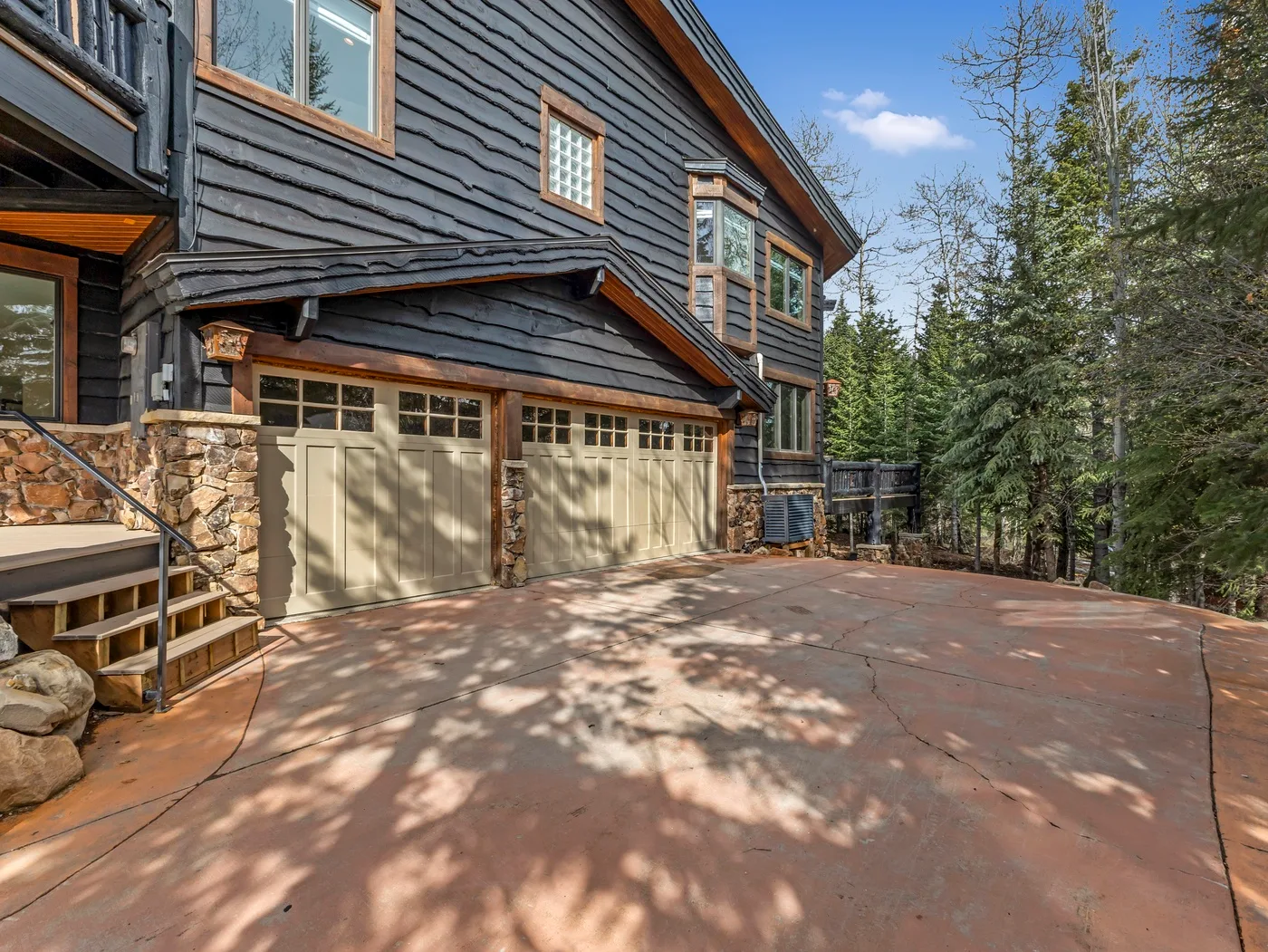 A mountain-style house with two garage doors beside a broad paved driveway.