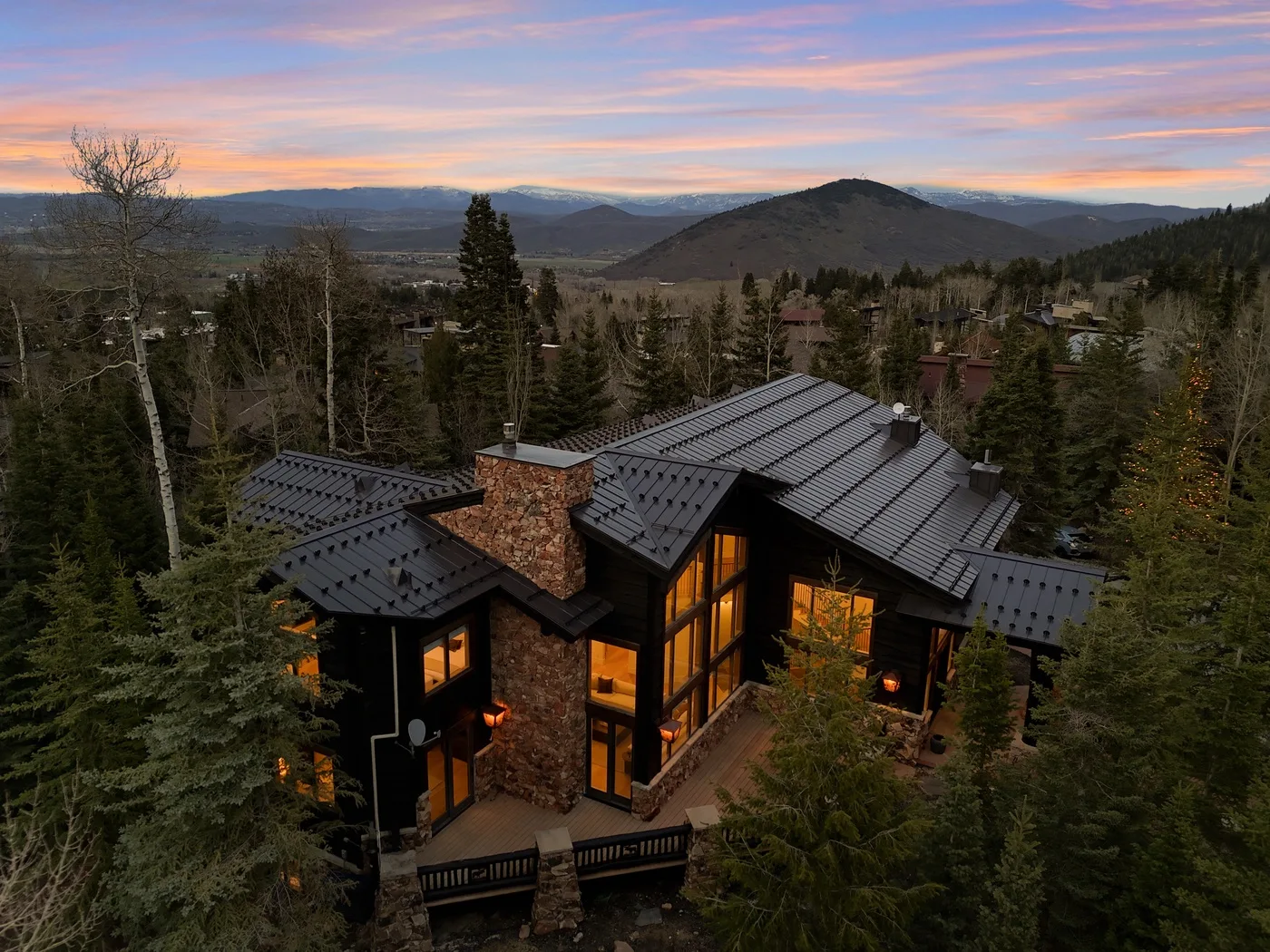 A large home sits among evergreen trees beneath a colorful sunset sky.