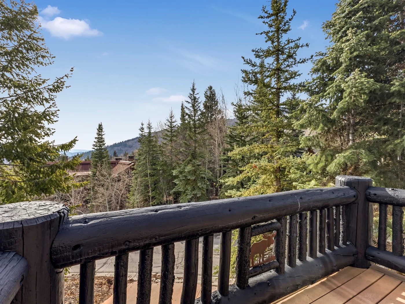A wooden deck railing overlooks a forested mountain landscape under a clear sky.