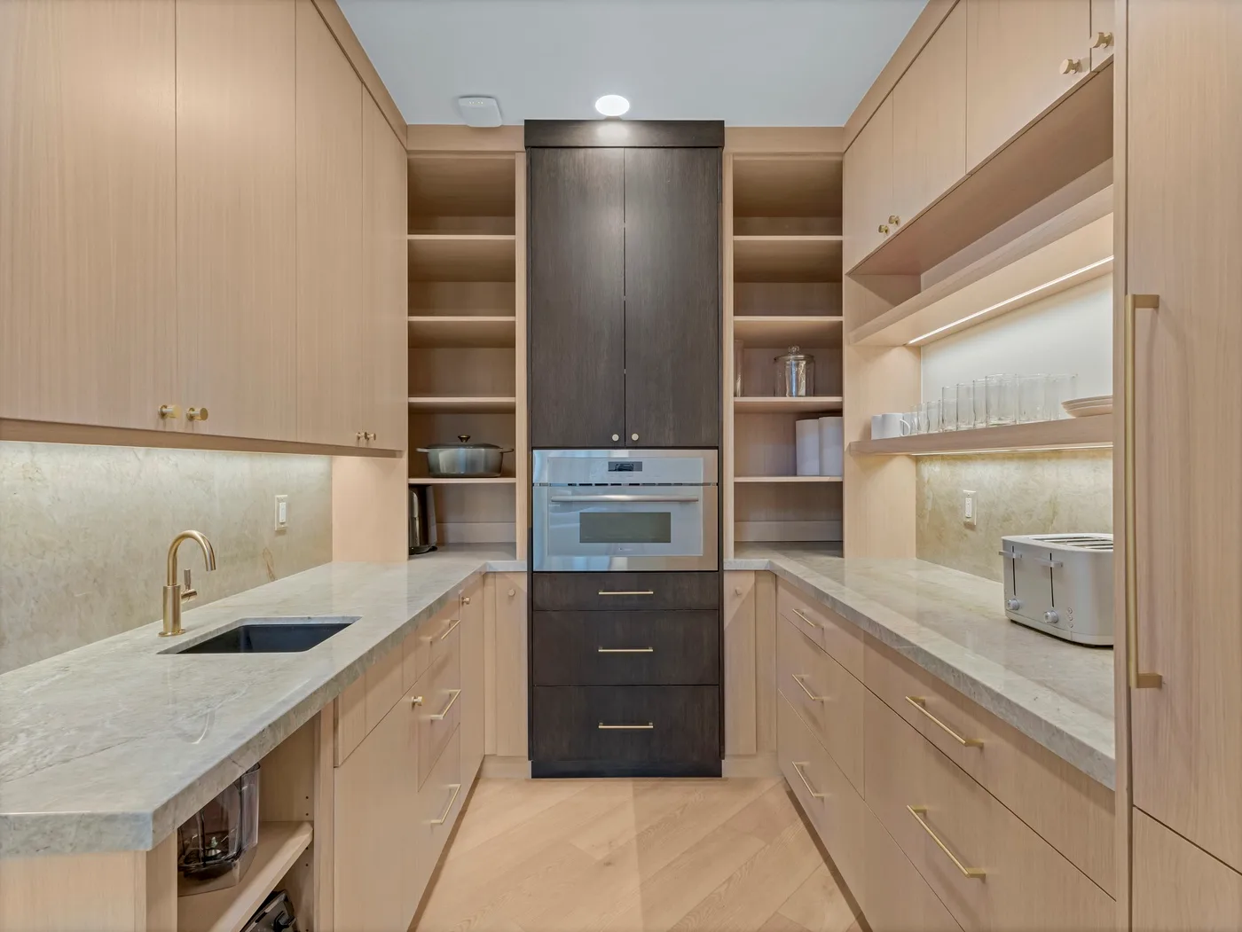 A modern kitchen with light wood cabinetry, stone counters, and built-in appliances.