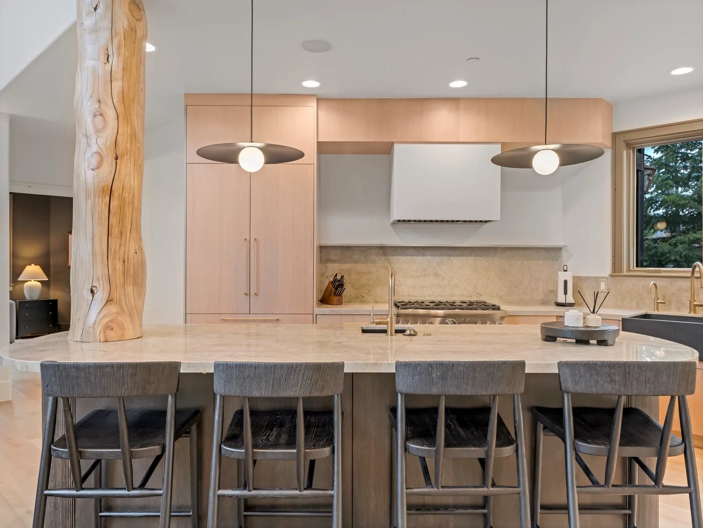 A modern kitchen with a broad island and stools beneath pendant lights.