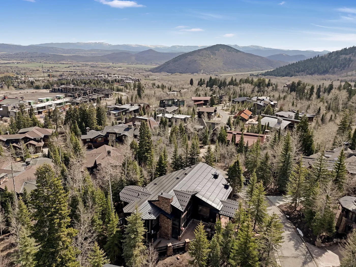 An aerial view of a forested residential area with mountains in the distance.
