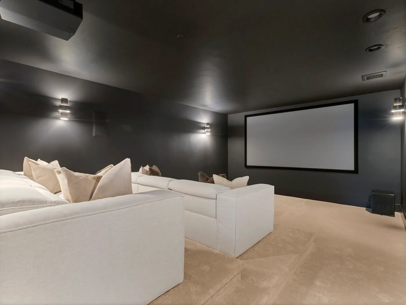 A home theater with white seating facing a large projection screen.