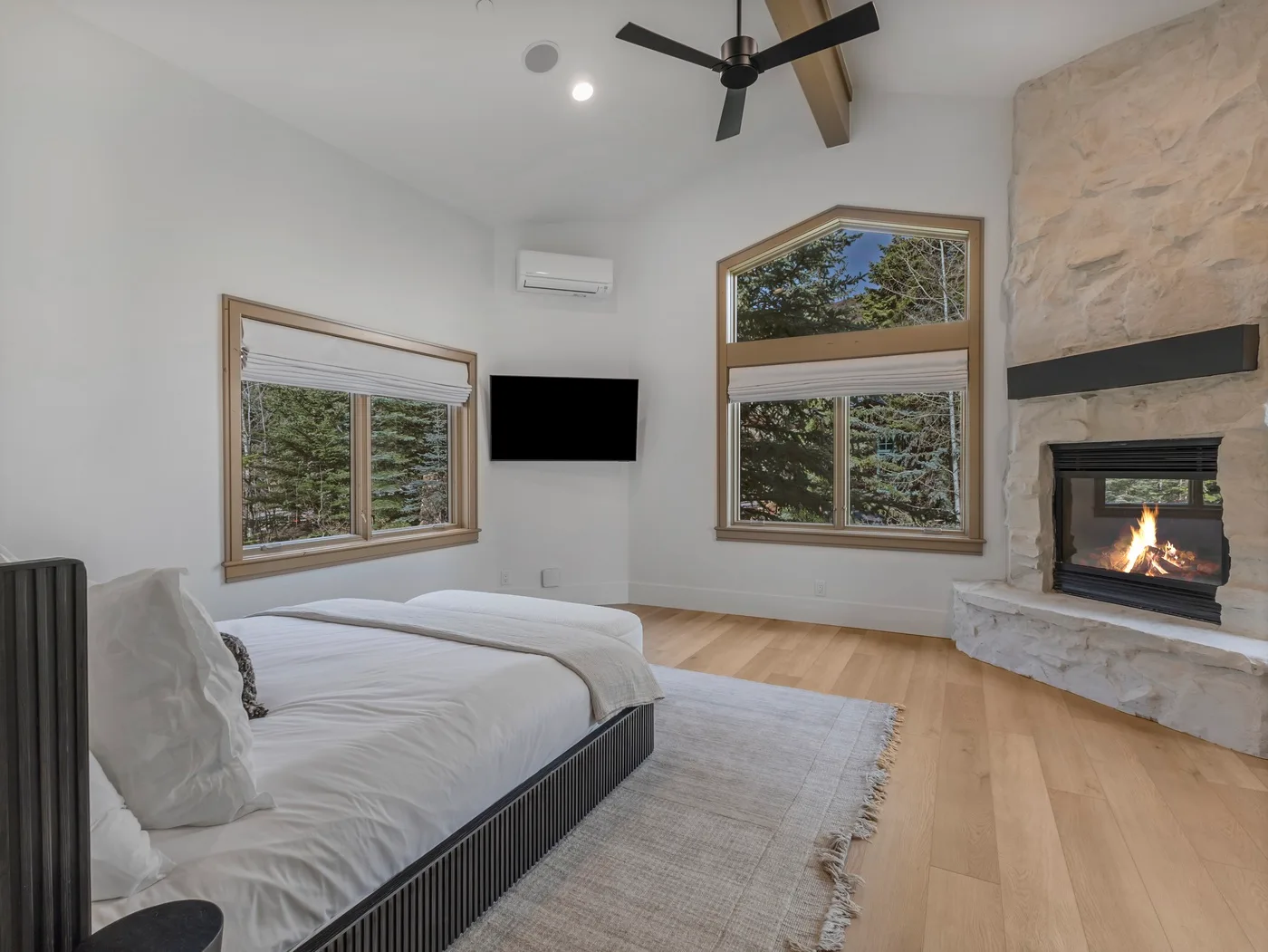 A bedroom with a low bed, large windows, and a lit fireplace.