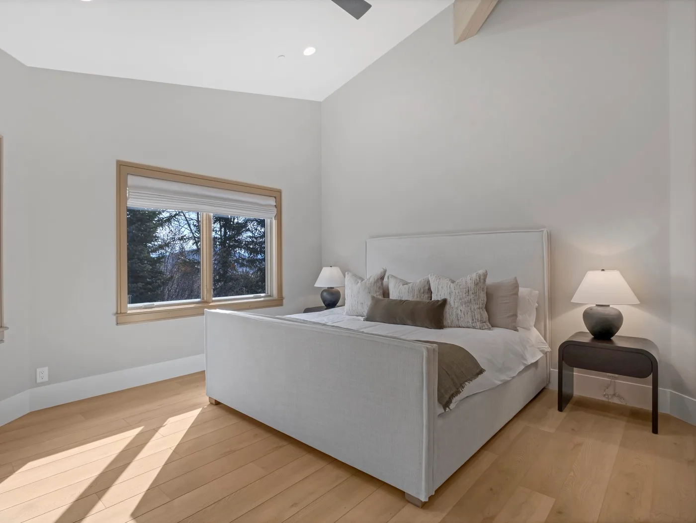 A bedroom with a neatly made bed, bedside lamps, and a large window.