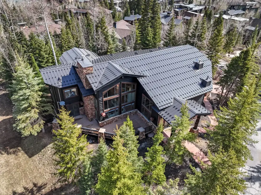 Aerial view of a large house with a dark roof among trees.