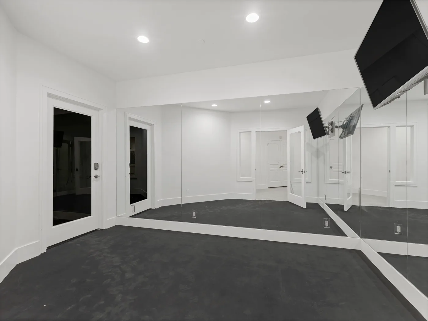 A spacious room with dark flooring, mirrored walls, and a wall-mounted television.