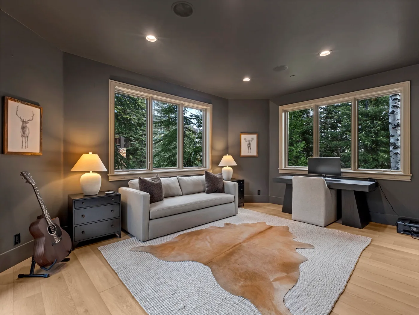 A living room with a sofa, large windows, and a desk overlooking trees.