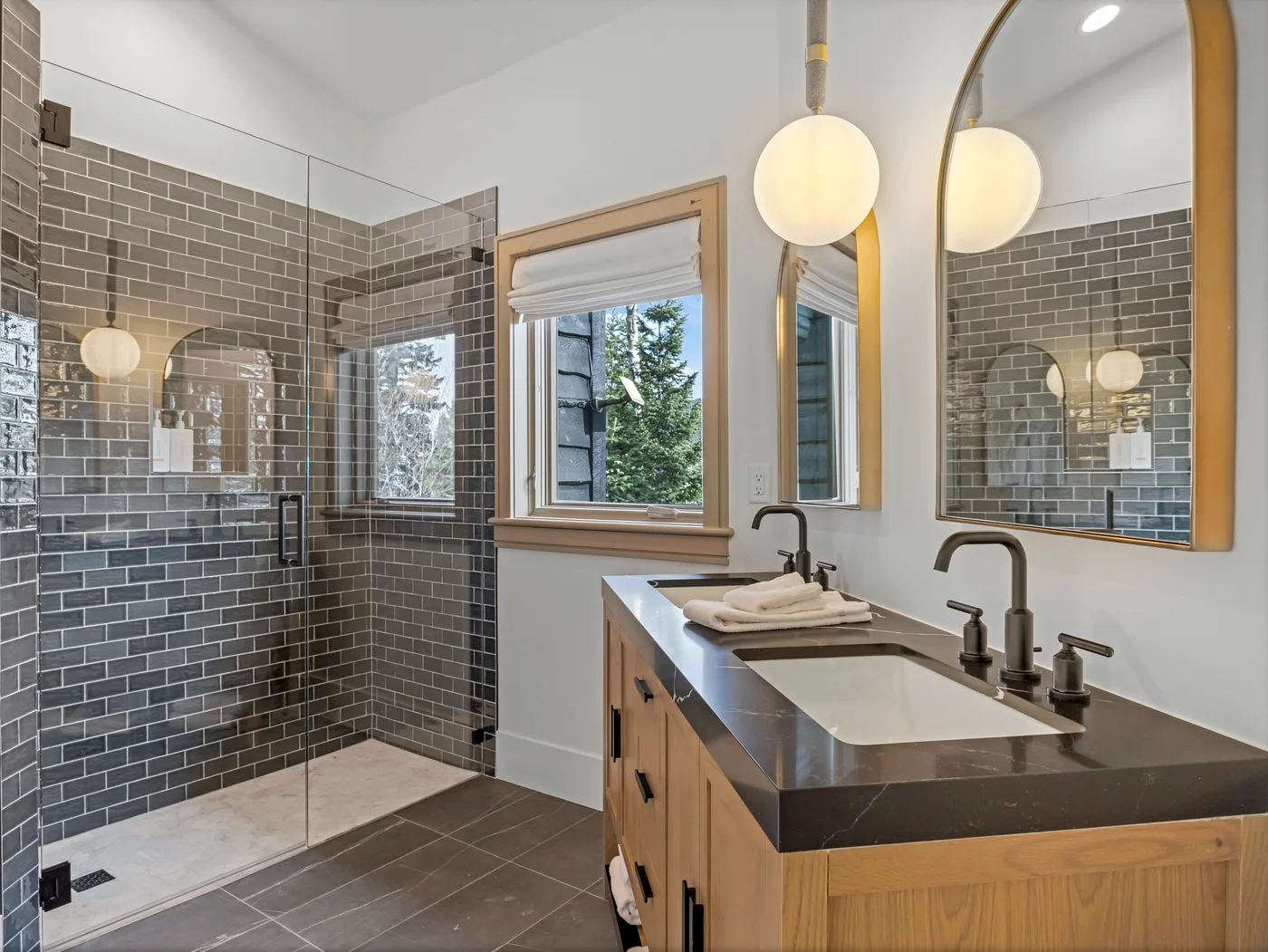 A tiled bathroom with a glass shower, a wooden vanity, and a large mirror.