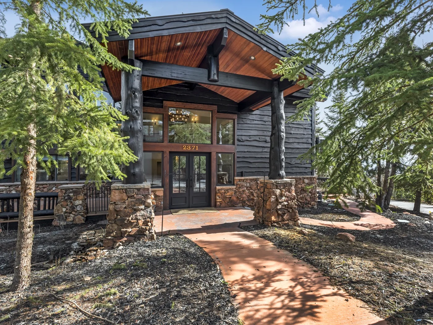 A dark timber building entrance sits beneath a broad wooden canopy, framed by trees.
