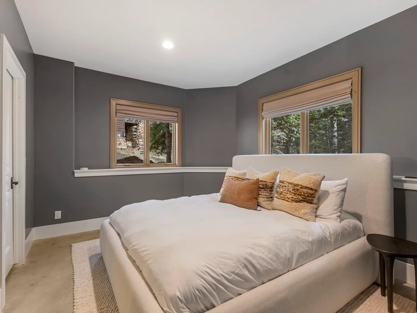 A bedroom with a bed, decorative pillows, and two windows.