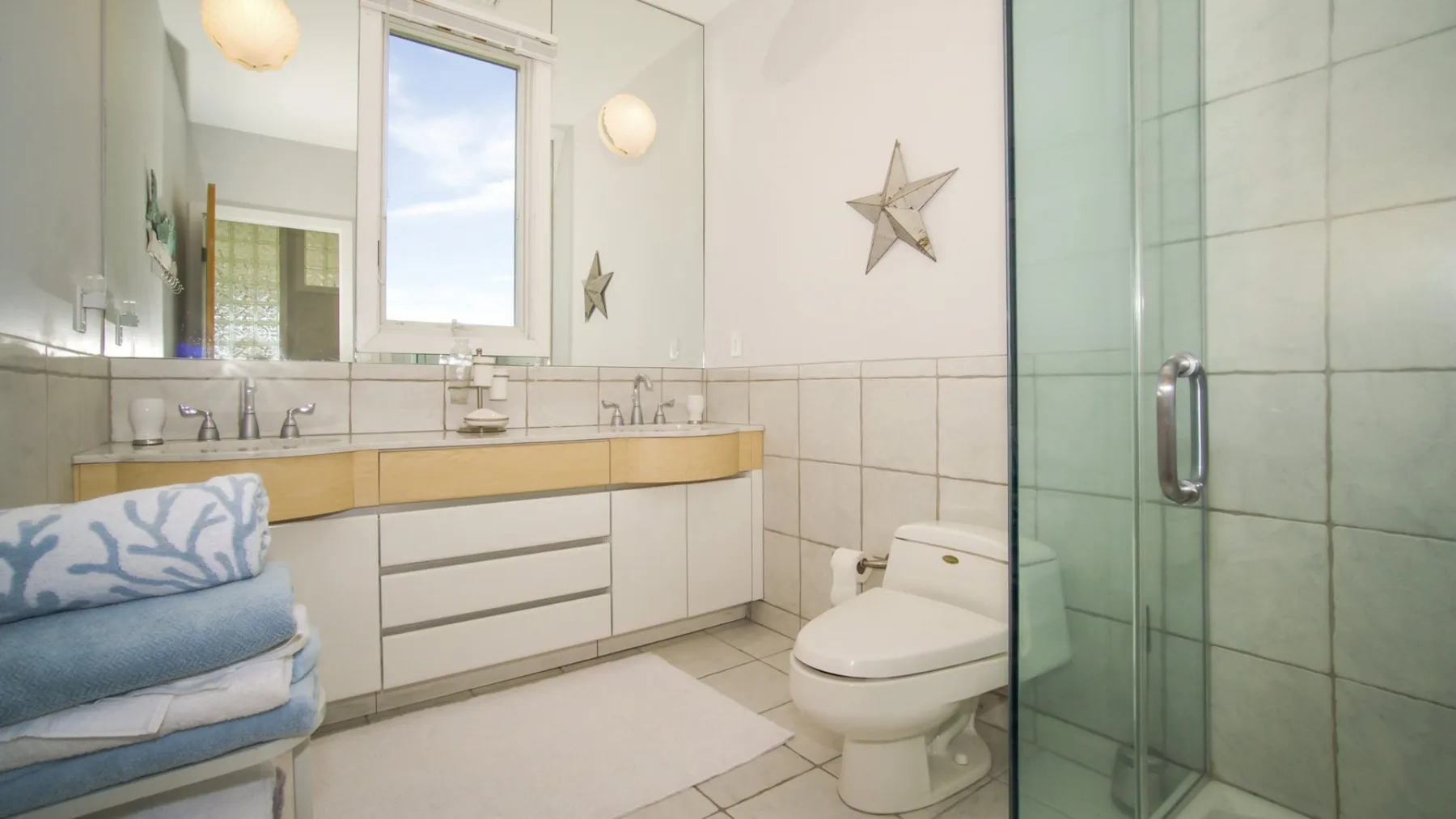 Un baño luminoso con un tocador largo, un inodoro y una ducha de vidrio.