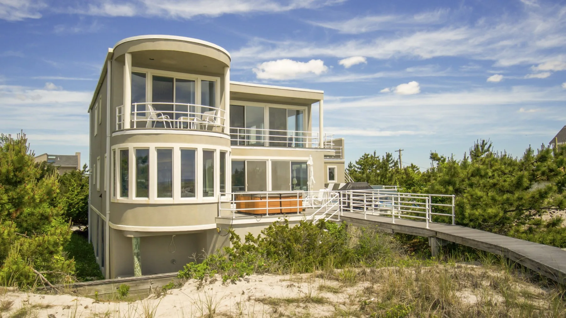 Una casa costera moderna con grandes ventanas y un paso elevado entre la vegetación.