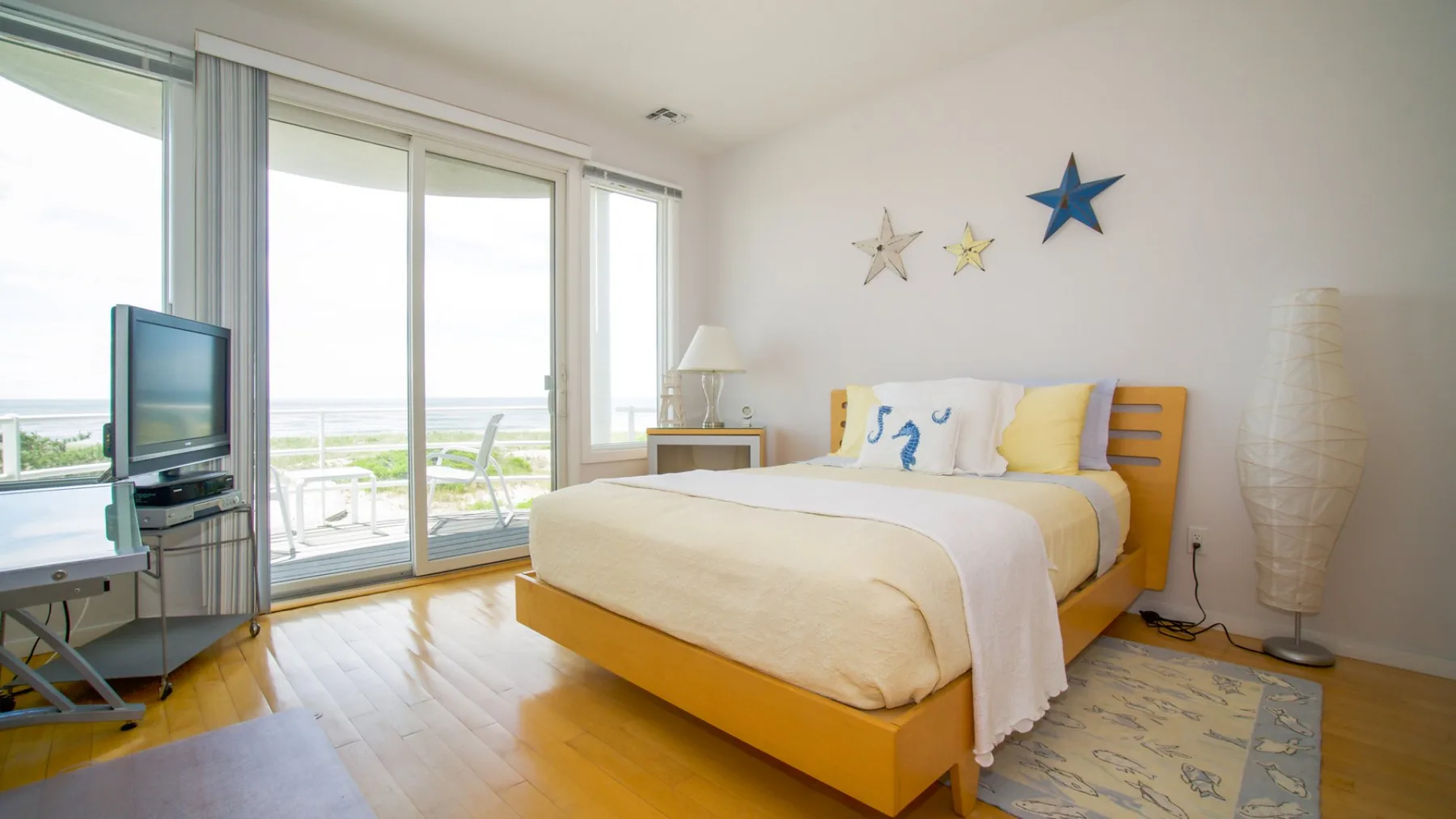 Un dormitorio con una cama, ventanas grandes y un televisor.
