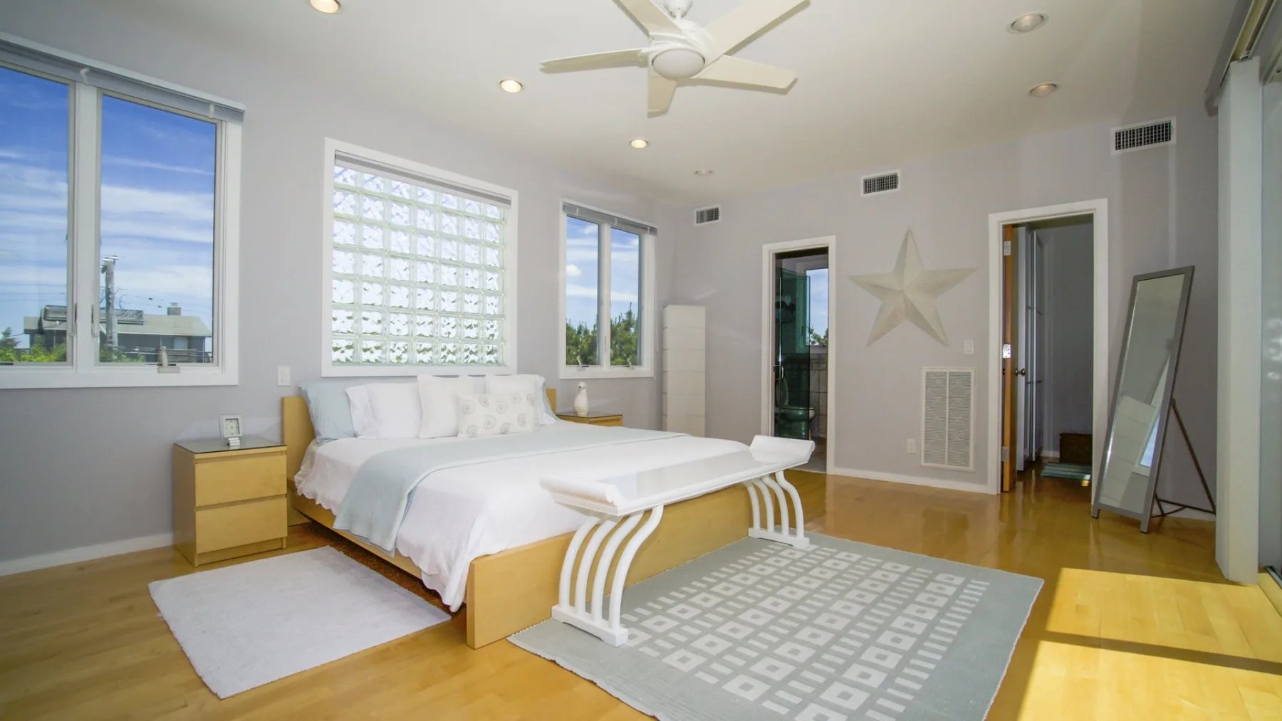 Un dormitorio luminoso con una cama, ventanas grandes y un ventilador de techo.