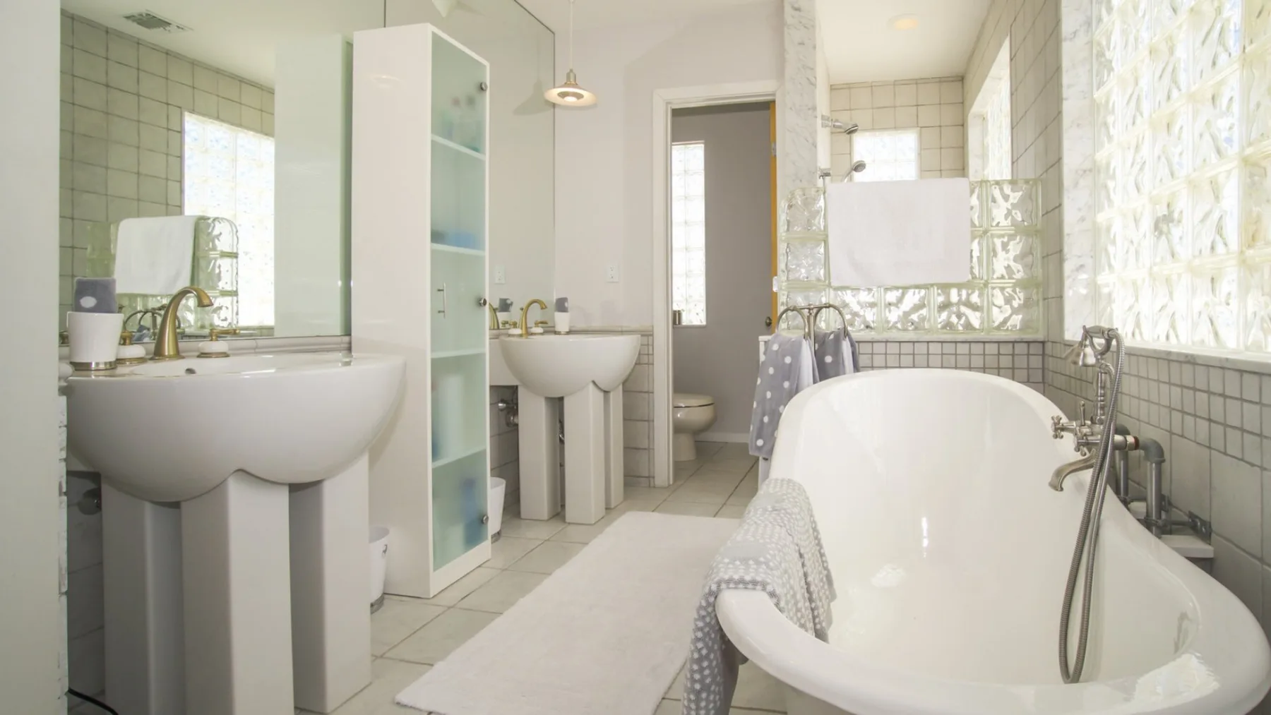 Un baño luminoso con bañera, lavabos y una zona de ducha acristalada.