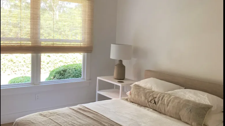 Dormitorio con una cama junto a una ventana grande y una pequeña mesa de noche.
