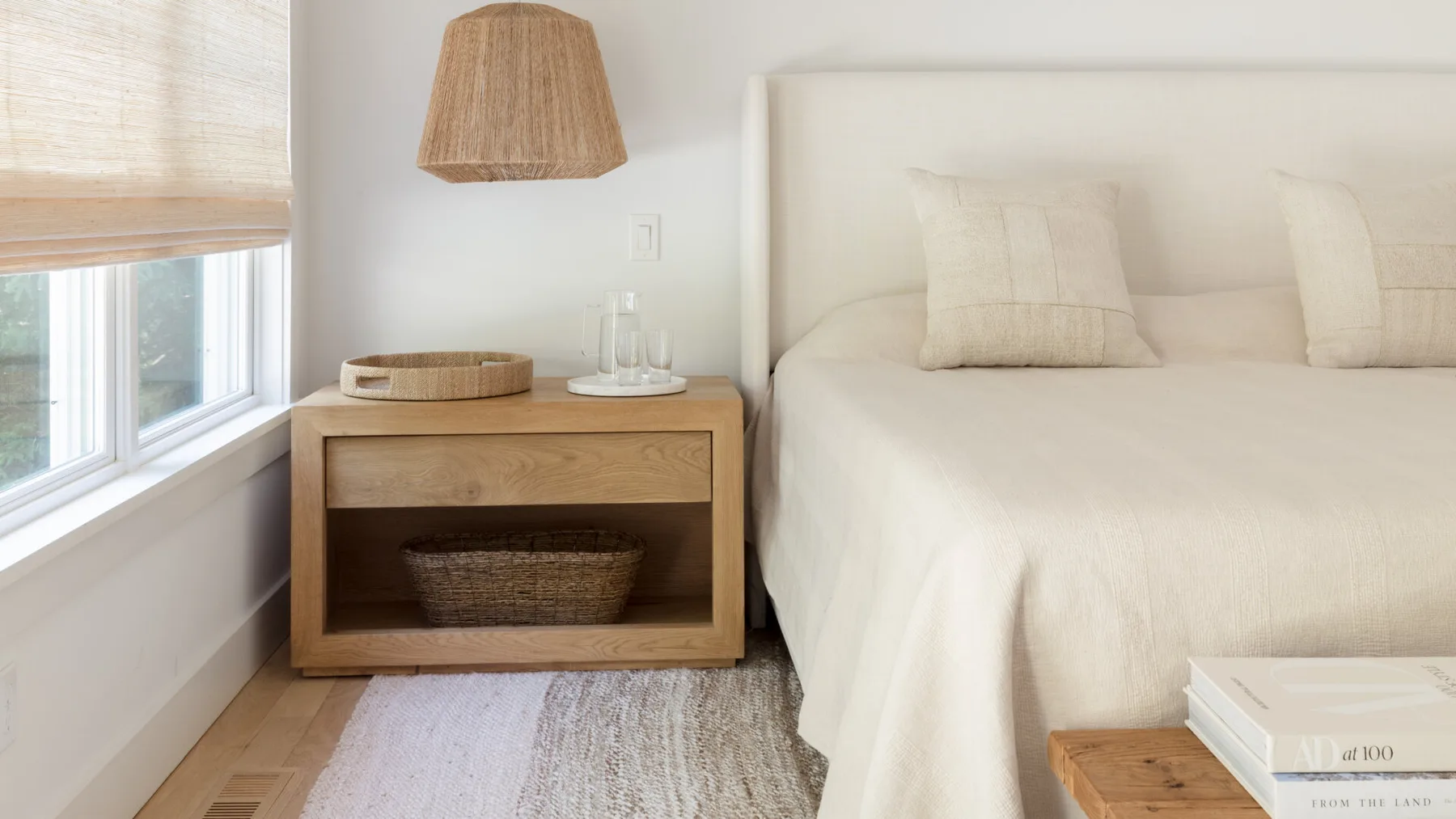 Un dormitorio luminoso con una cama bien tendida junto a una mesita de madera.