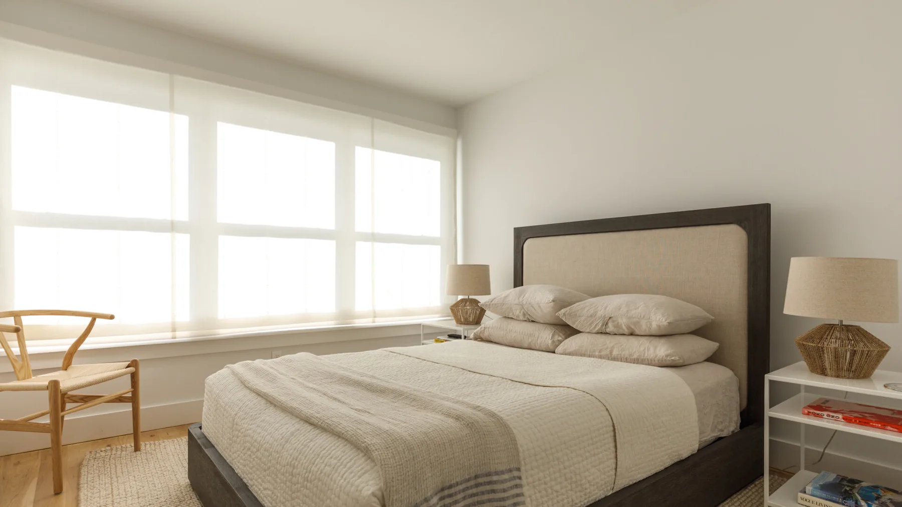 Un dormitorio luminoso con una cama bien arreglada junto a grandes ventanas.