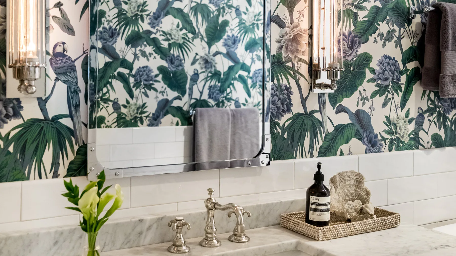 Un lavabo de baño con espejo, papel tapiz estampado y grifo.
