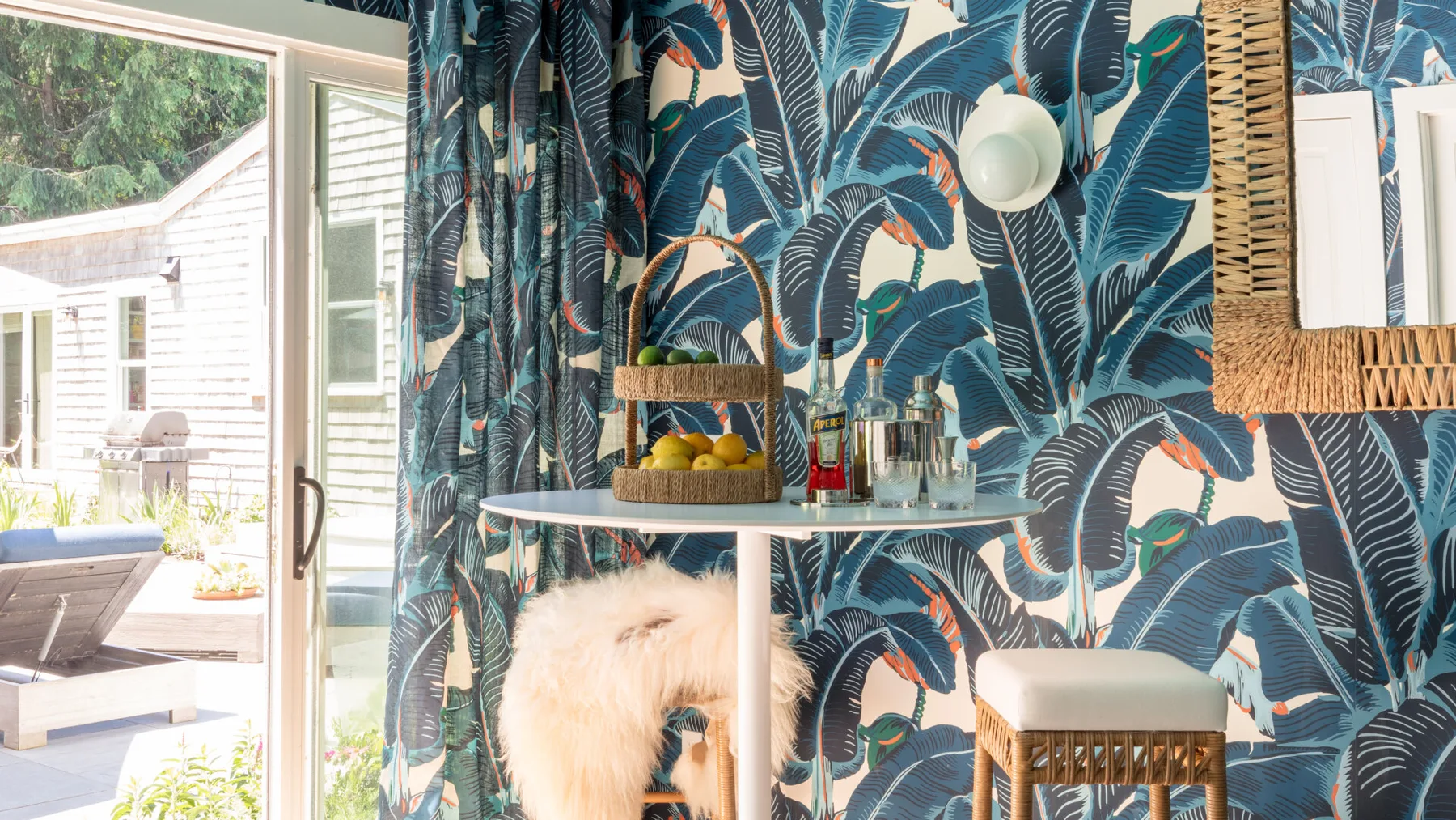 Un comedor con una mesa pequeña y cortinas de estampado tropical junto a una puerta de vidrio abierta.