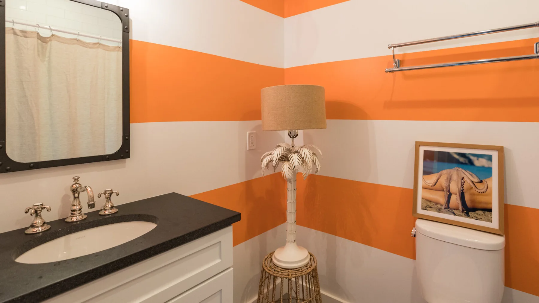Un baño con lavabo, inodoro y llamativas franjas naranjas y blancas en las paredes.