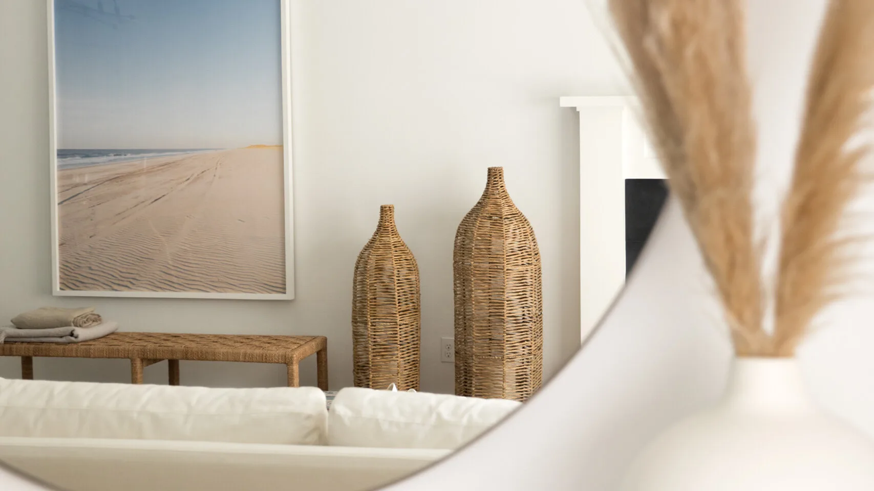 Una sala de estar en tonos neutros tiene una foto enmarcada de una playa y jarrones decorativos tejidos.