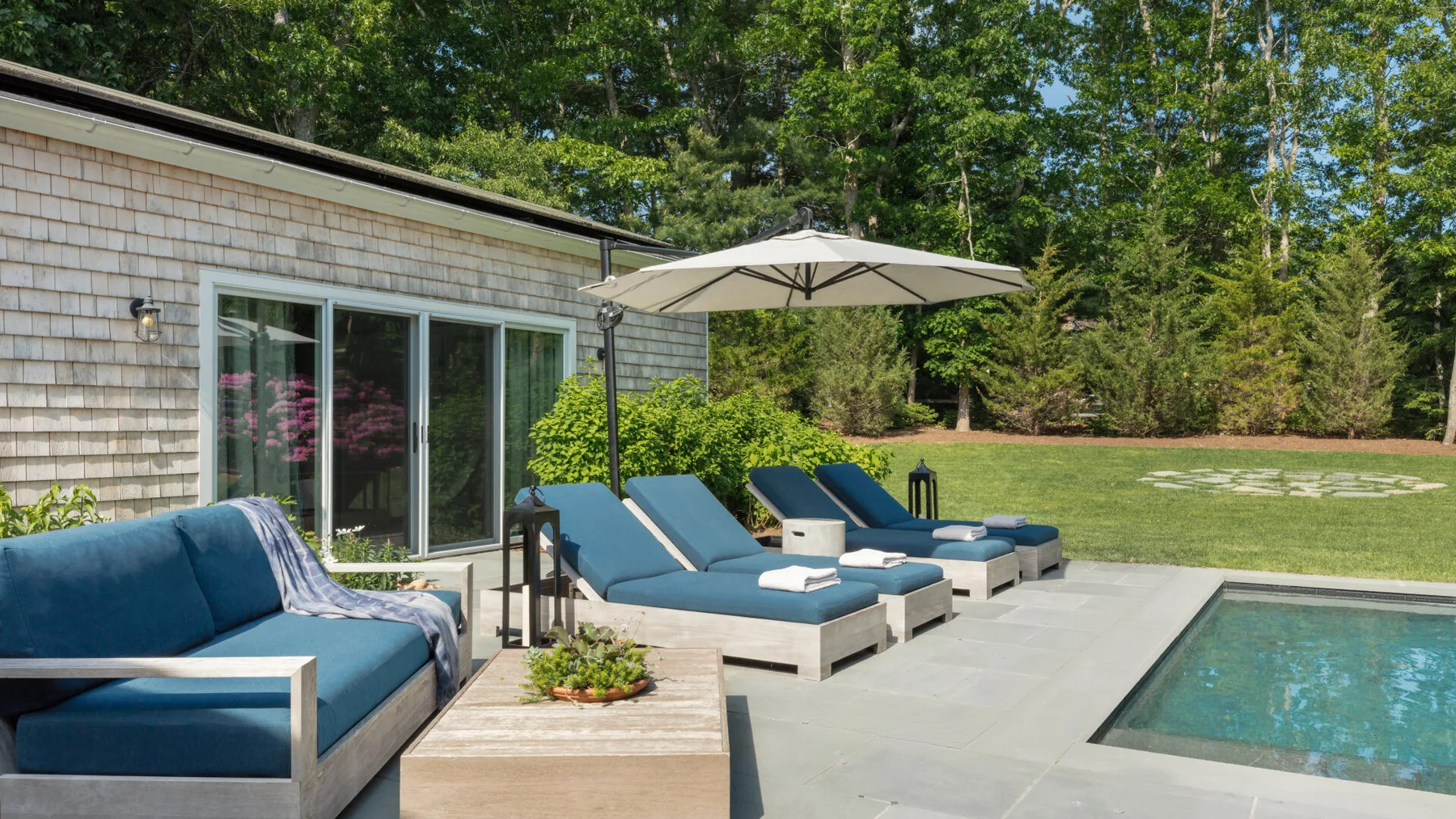Un patio exterior con asientos acolchados, una sombrilla y una piscina.