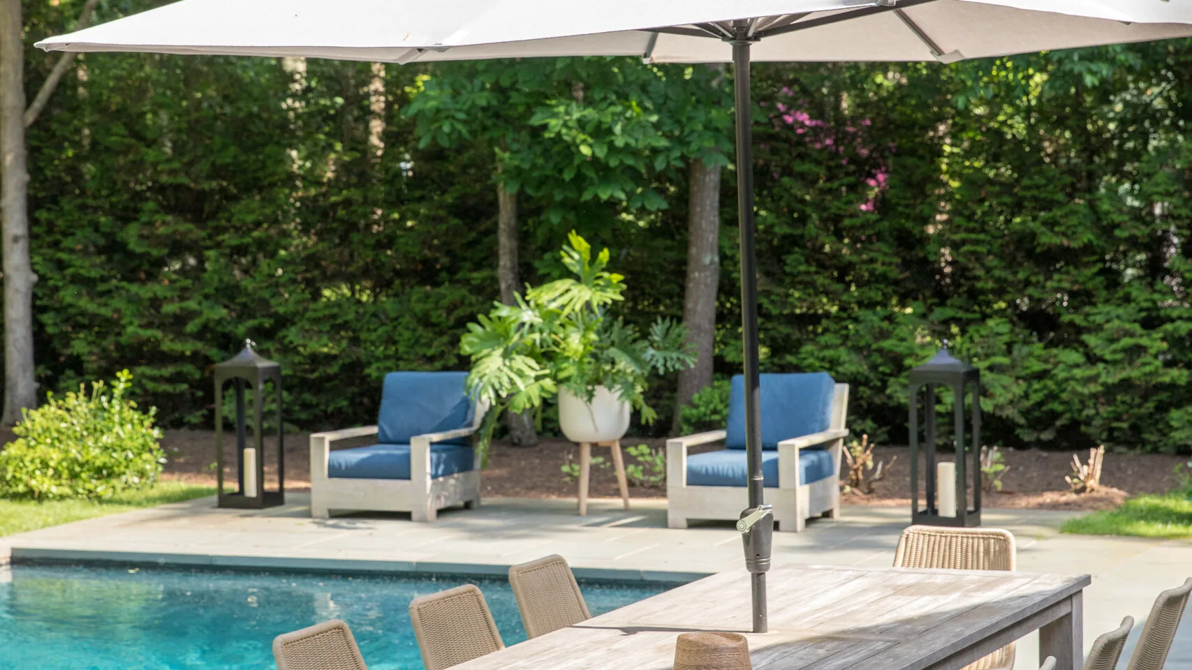 Una zona exterior junto a la piscina, con una mesa bajo una sombrilla grande.