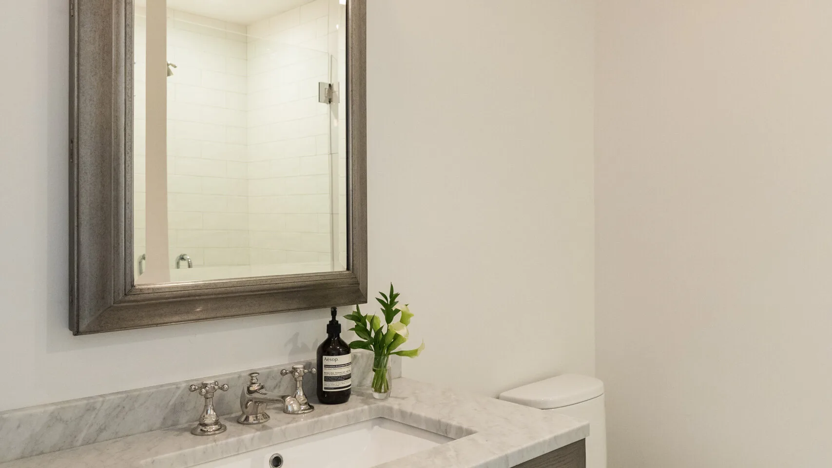 Un lavabo de baño con espejo enmarcado, fregadero y un pequeño jarrón con flores.
