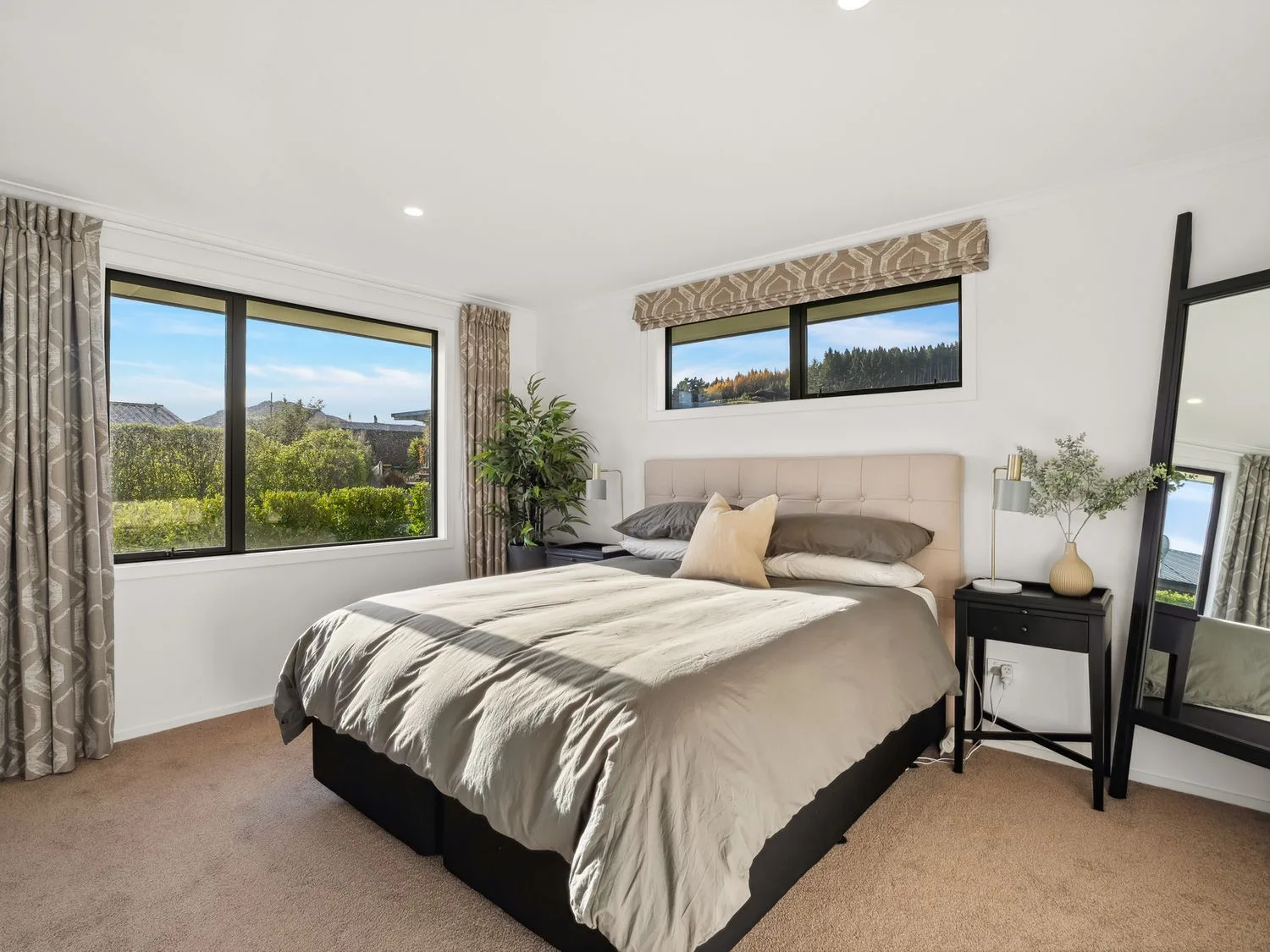 A bright bedroom with a bed, bedside table, and large windows.