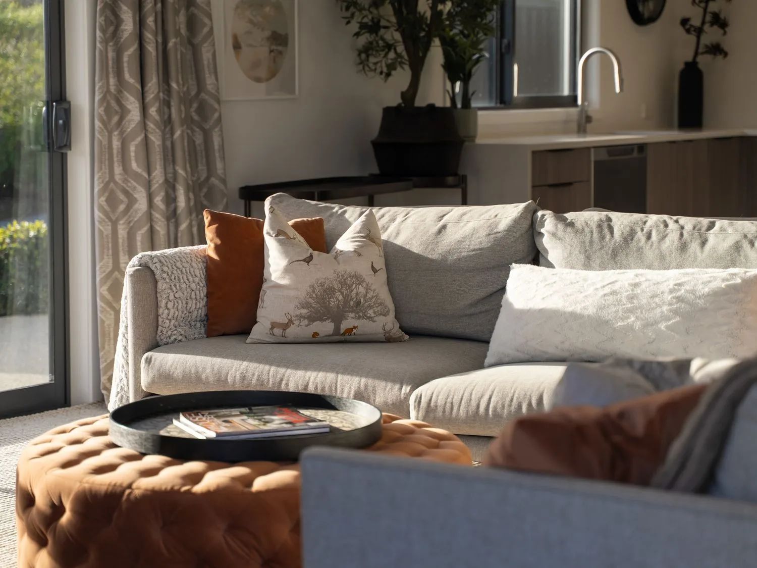 A living room with a sofa and a round tray on a cushioned ottoman.