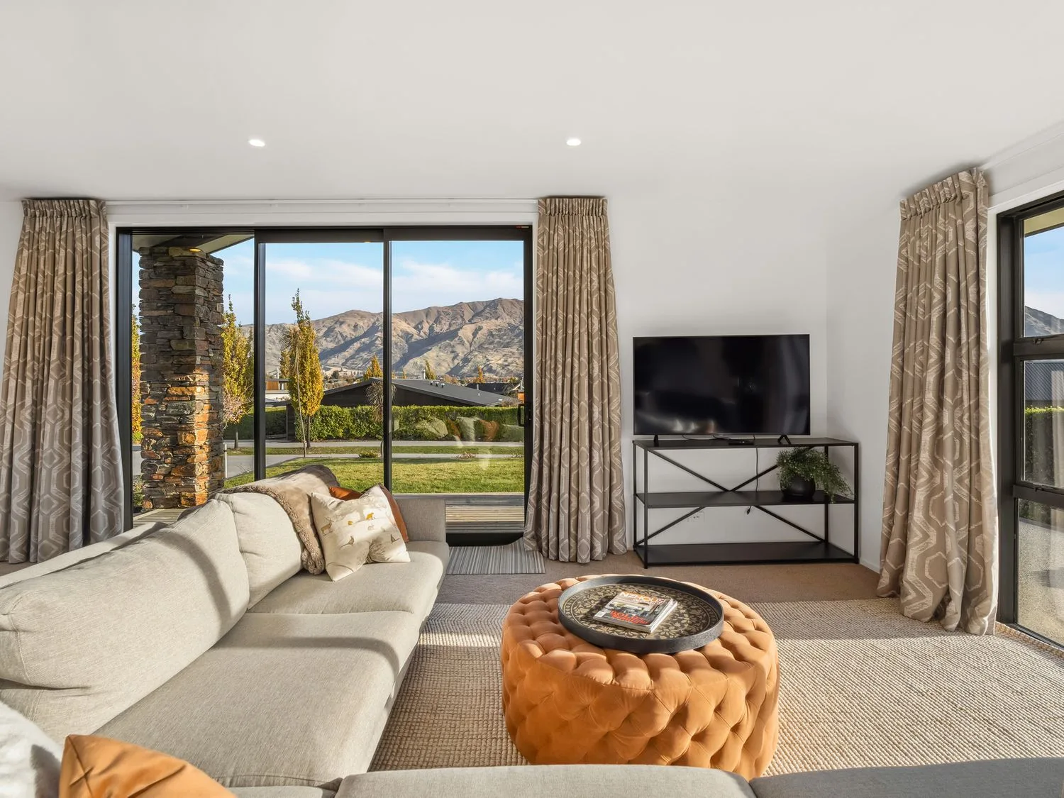 A living room with seating, a television, and a view of mountains through glass doors.