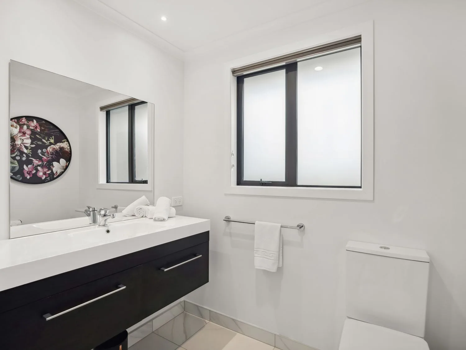 A bright bathroom with a sink, toilet, and window.