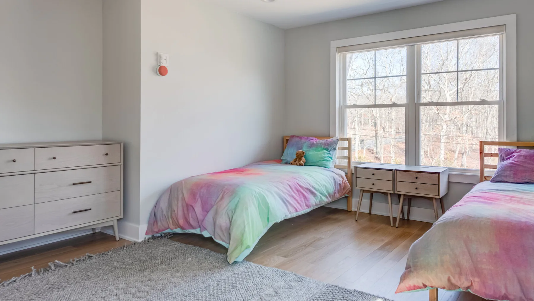 Un dormitorio luminoso con dos camas, una ventana grande y una mesita de noche.
