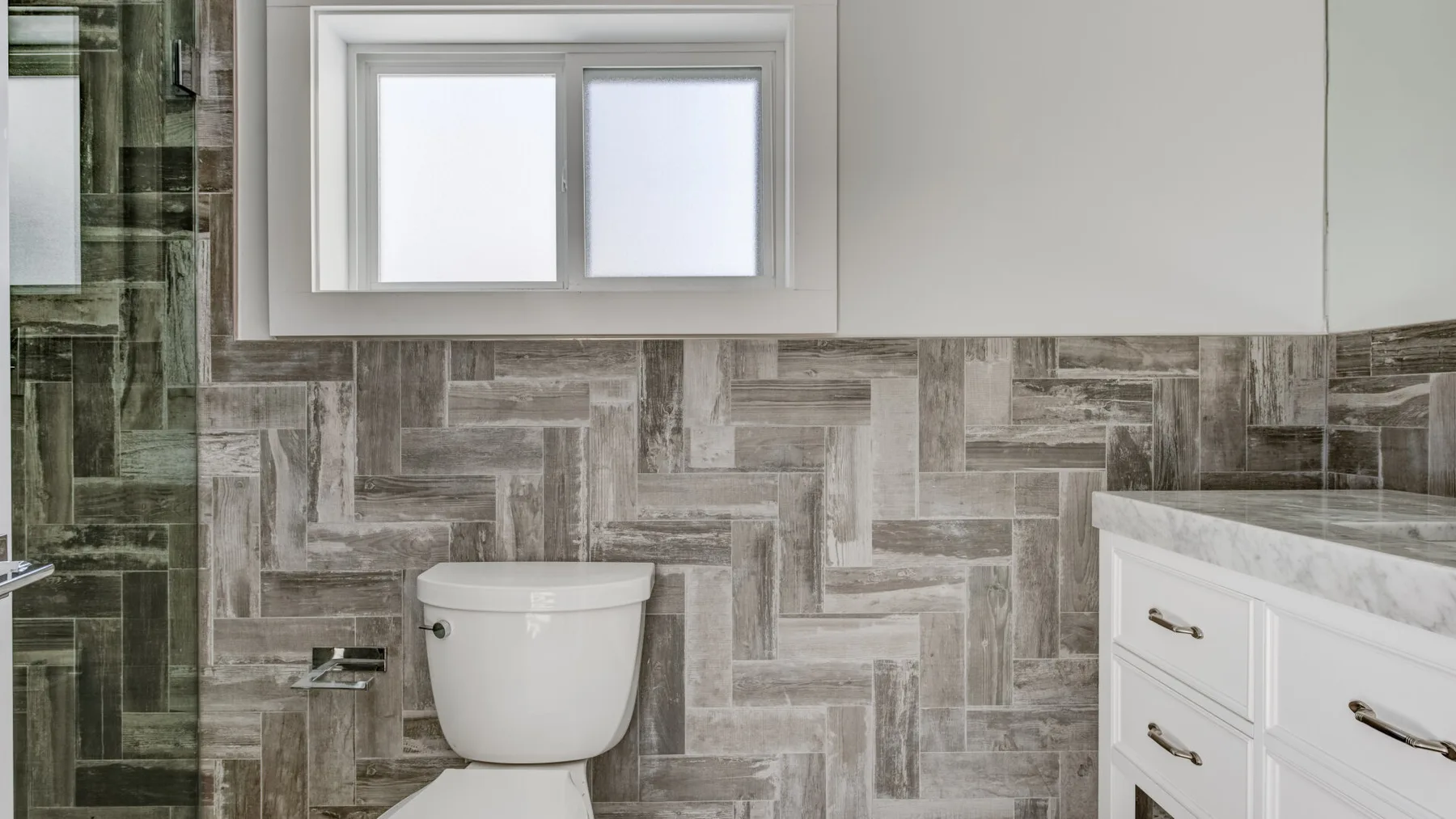 Un baño con un inodoro, una ventana y azulejos estampados.