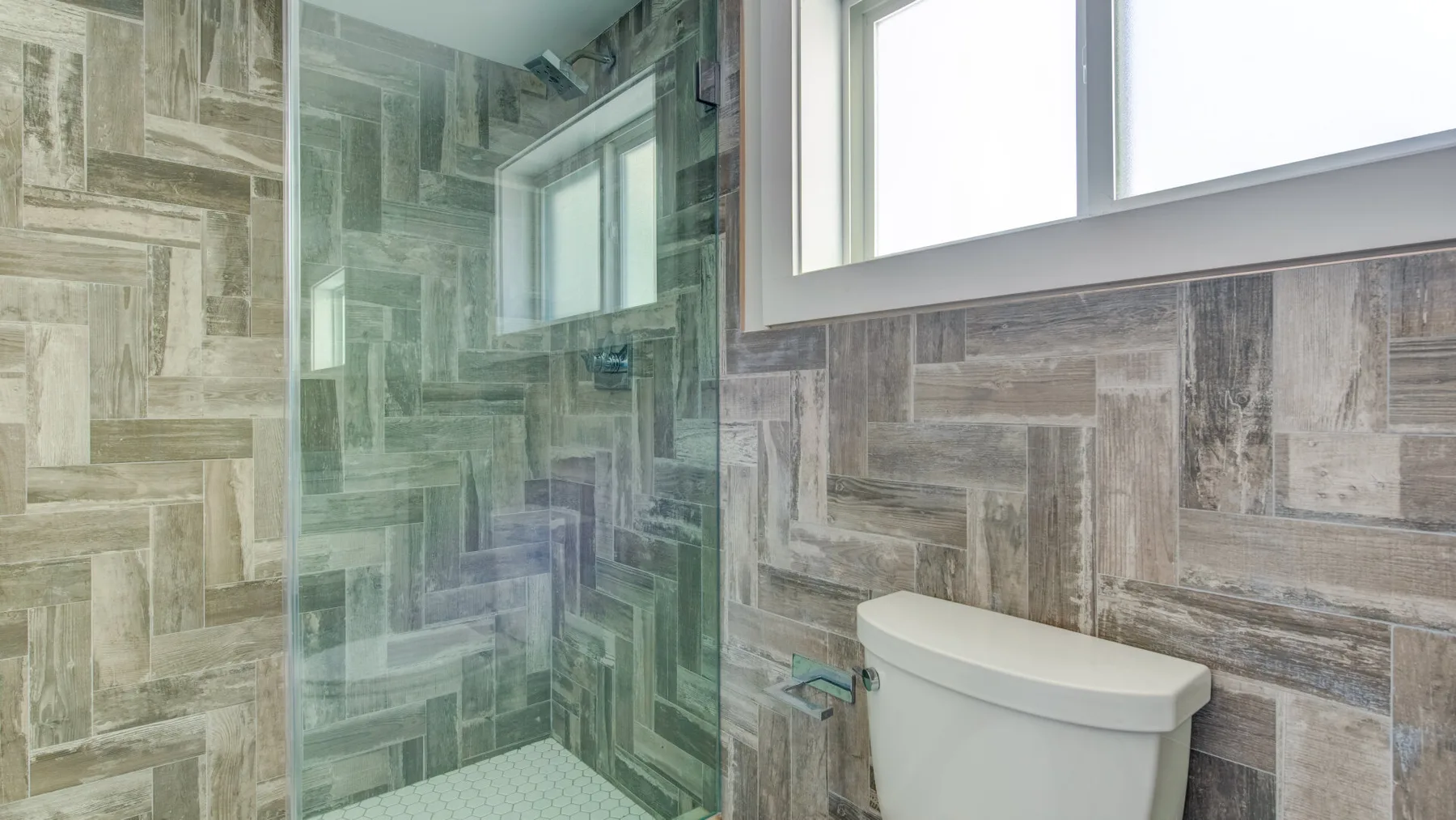 Un baño con azulejos, una ducha de vidrio y un inodoro bajo una ventana.