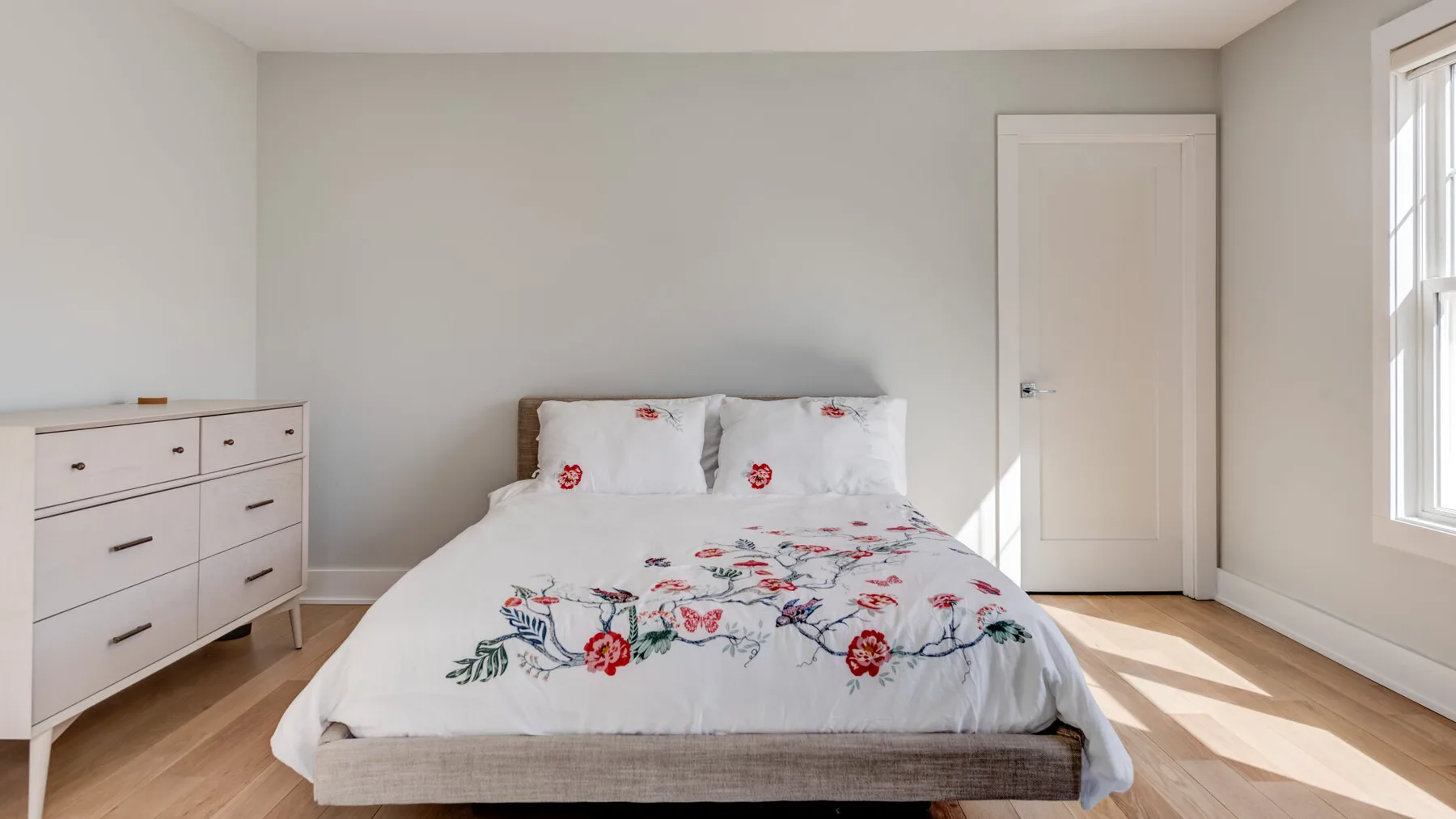Un dormitorio con una cama cubierta con ropa de cama floral y una cómoda al lado.