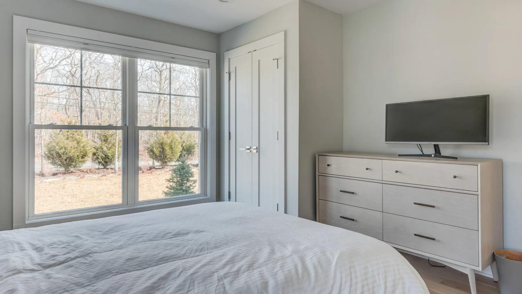 Un dormitorio con una cama, una cómoda y un televisor junto a una ventana grande.