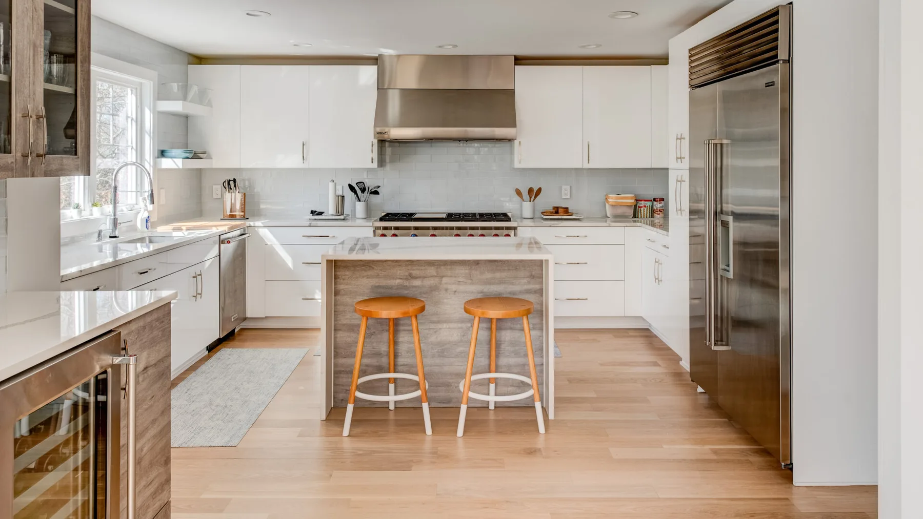 Una cocina moderna y luminosa con gabinetes blancos y una isla central con taburetes.