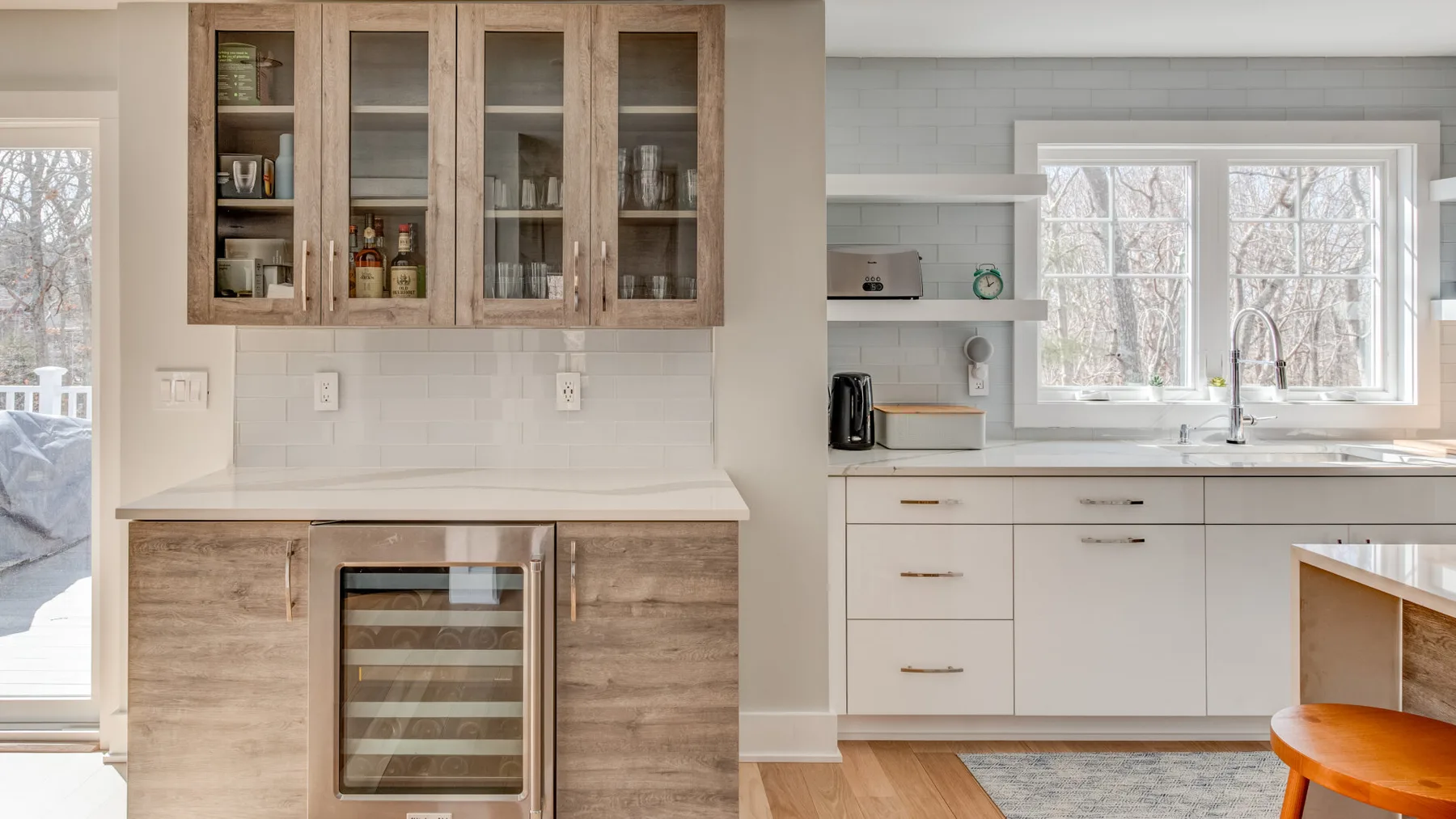 Una cocina luminosa con gabinetes claros, una nevera para bebidas con puerta de vidrio y una ventana amplia.