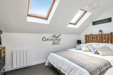 A bright bedroom with a bed beneath two skylights and a wooden headboard.
