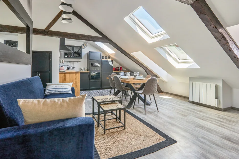 An open-plan living area and kitchen with a dining table beneath skylights.