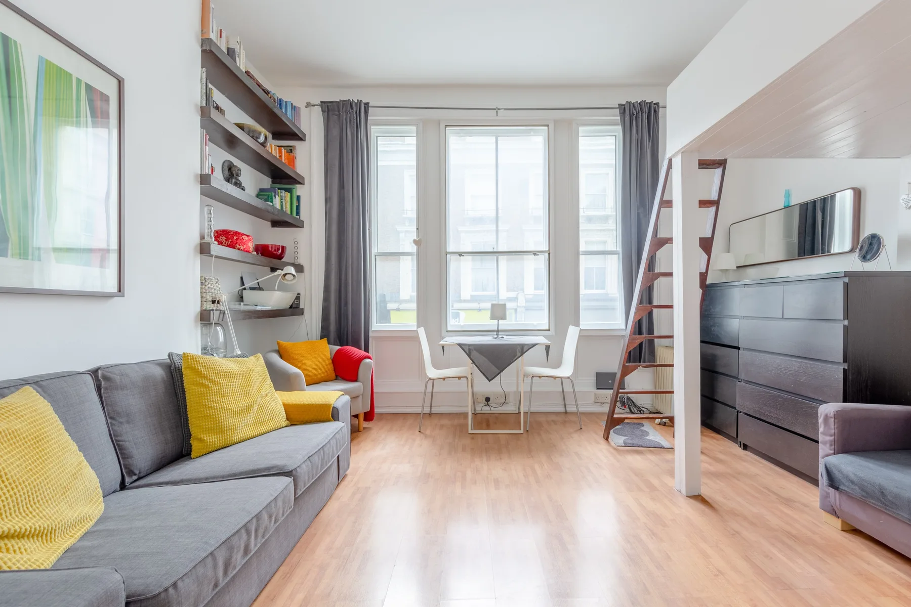 A bright living room with gray seating, wall shelves, and large windows.