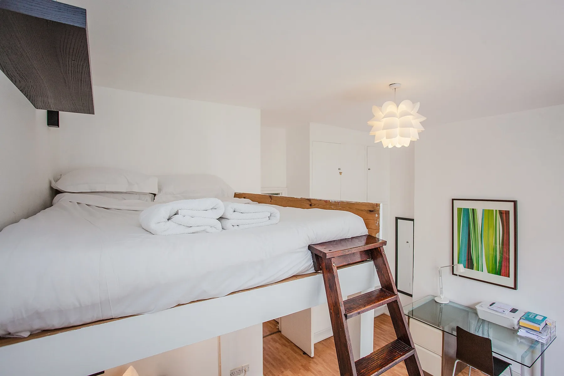 A bright bedroom with a raised bed and a colorful framed artwork.